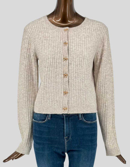  Authentic screen-worn Icône par Simons cream ribbed-knit cardigan featuring charming gold-tone bow button details. Classic crew neck design with long sleeves and fitted silhouette. 