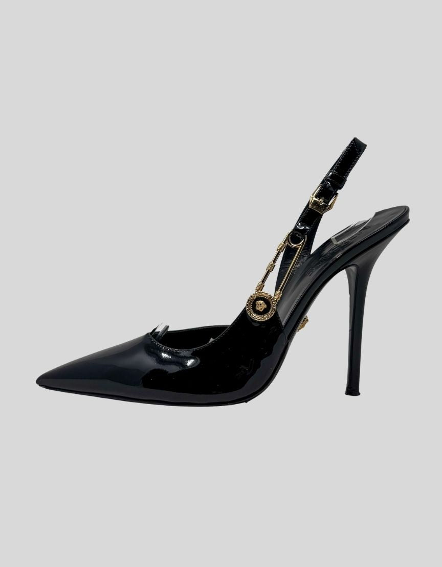 VERSACE safety pin slingback pumps in black patent leather. Features pointed toe silhouette, signature gold-tone Medusa safety pin hardware at slingback strap, stiletto heel. 