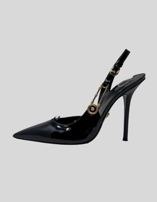 VERSACE safety pin slingback pumps in black patent leather. Features pointed toe silhouette, signature gold-tone Medusa safety pin hardware at slingback strap, stiletto heel. 