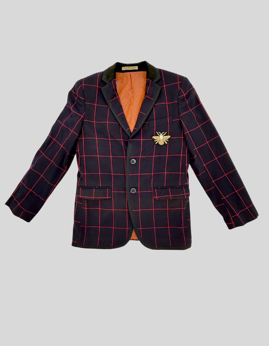 ROMANO LUXURY COLLECTION three-piece suit for boys in navy windowpane check. Hand-tailored. This formal ensemble includes a fully-lined jacket with golden bee brooch detail, a matching waistcoat vest with contrast orange polka dot backing, and tailored trousers.