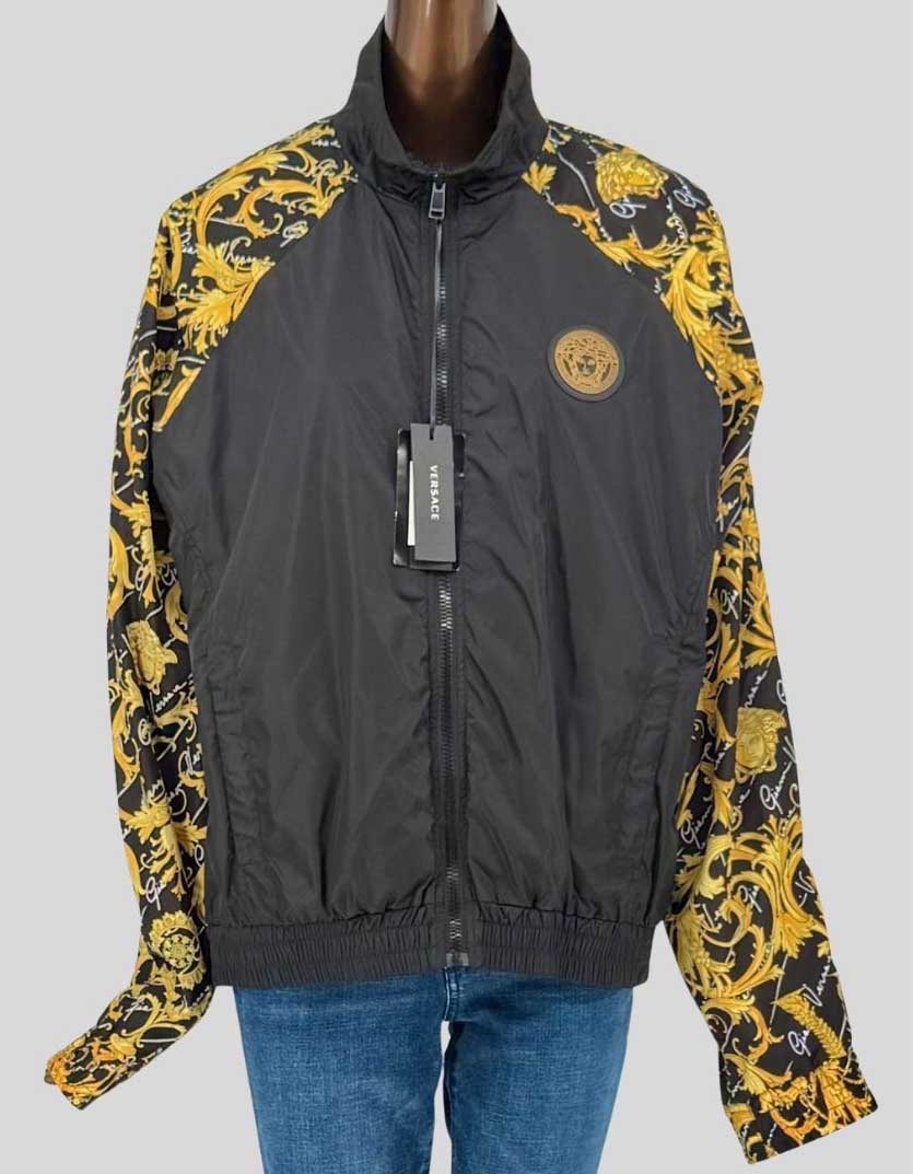 VERSACE iconic baroque print windbreaker featuring signature gold Medusa medallion logo. Black nylon body with contrast baroque print sleeves in signature gold and black design. Lightweight construction with mesh lining, stand collar, and full zip closure. Ribbed cuffs and hem for athletic fit. 
