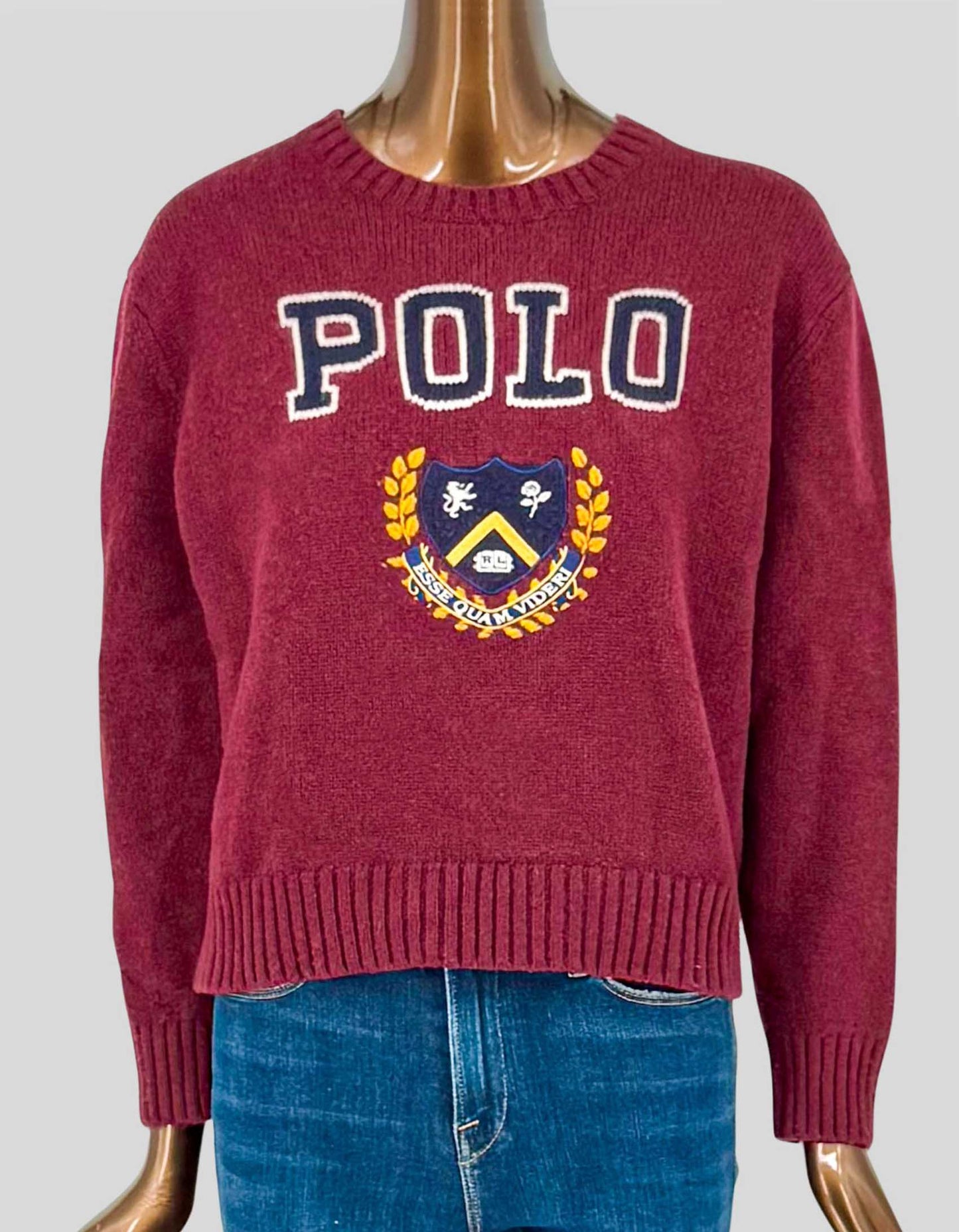 POLO RALPH LAUREN crew neck sweater in rich burgundy featuring bold "POLO" lettering and classic crest emblem at front. Made from 100% wool for warmth and durability. The collegiate-inspired graphic design showcases iconic Polo Ralph Lauren branding with embroidered crest details. Ribbed crew neck, cuffs, and hem provide structure and classic finishing. A preppy classic.