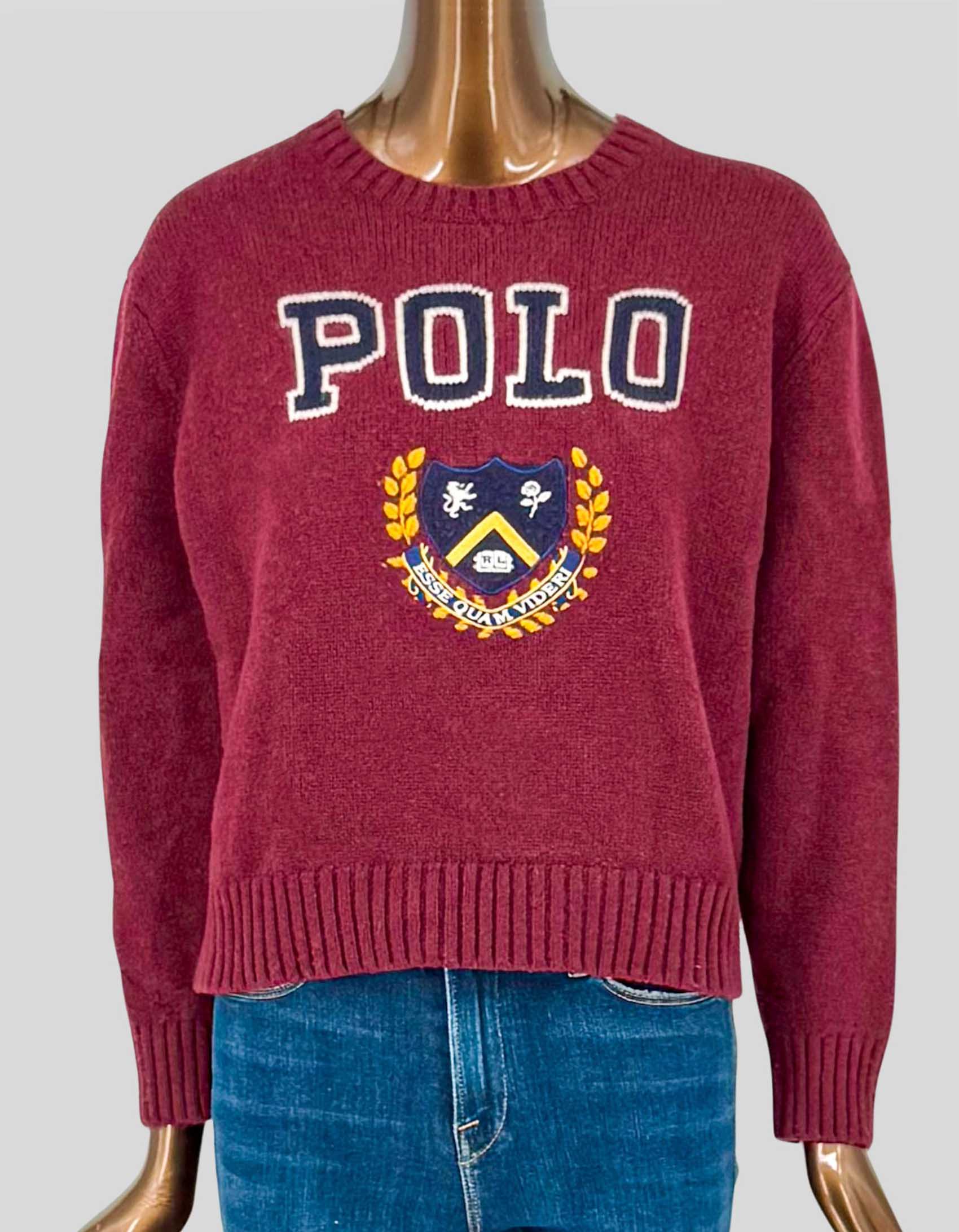 POLO RALPH LAUREN crew neck sweater in rich burgundy featuring bold "POLO" lettering and classic crest emblem at front. Made from 100% wool for warmth and durability. The collegiate-inspired graphic design showcases iconic Polo Ralph Lauren branding with embroidered crest details. Ribbed crew neck, cuffs, and hem provide structure and classic finishing. A preppy classic.